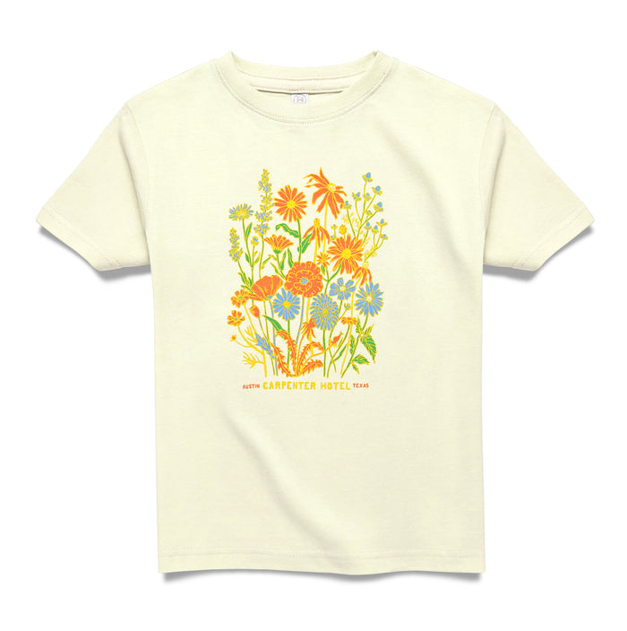 A beige kids' t-shirt with a colorful floral graphic design and text that says ' CARPENTER HOTEL AUSTIN TEXAS' on the chest