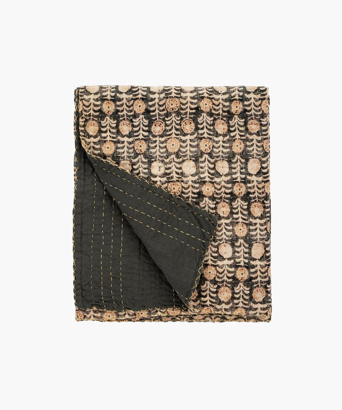 Folded throw blanket or quit with intricate patterns of beige circular floral motifs on a dark background. The corner reveals a contrasting black underside with yellow stitching. | Wildwood Home Co.
