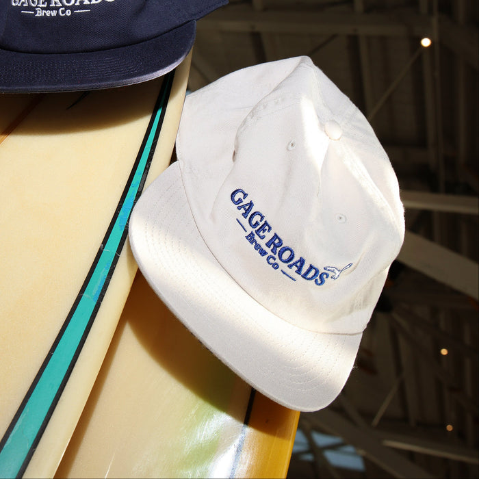 Two hats with 'Gage Roads' branding on a surfboard.