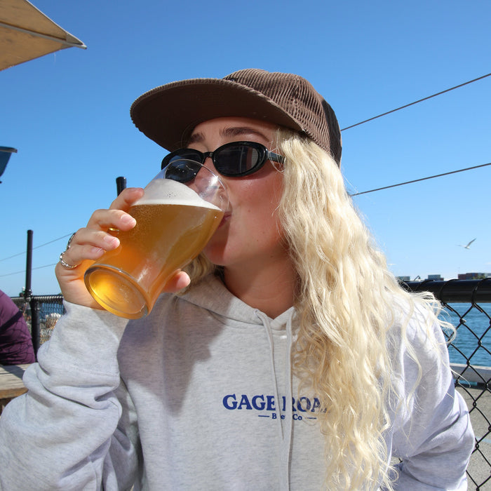 Person drinking beer outdoors wearing a 'Gage Road' hoodie