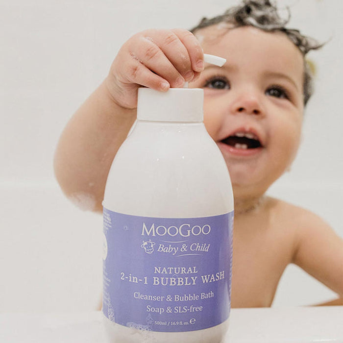 Child holding a bottle of Moogoo Baby & Child Natural Bubbly Wash in a bubble bath