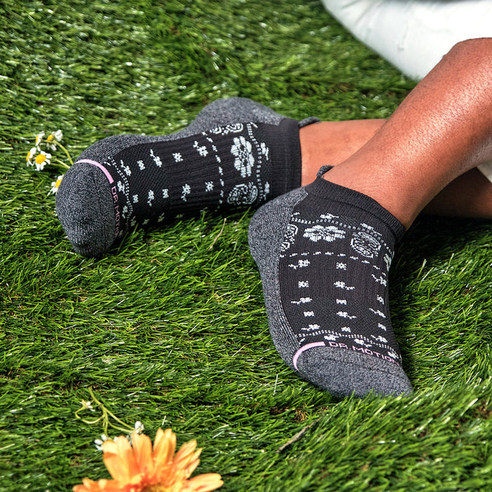 Black ankle compression socks with floral pattern, resting on grass with a flower nearby.