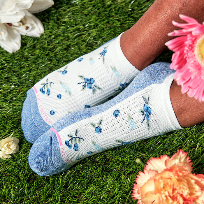 Ankle compression socks with a blue and white floral design, resting on green grass with flowers nearby.