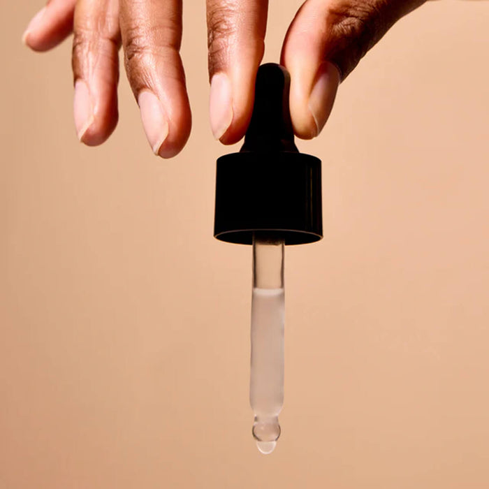 Hand holding black dropper against a tan background.