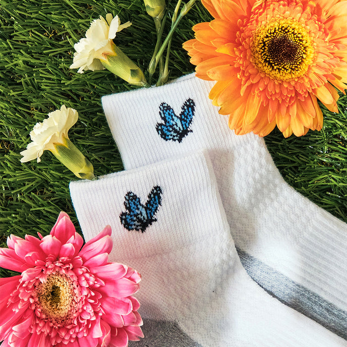 White quarter compression socks featuring a blue butterfly design, surrounded by colorful flowers on green grass.