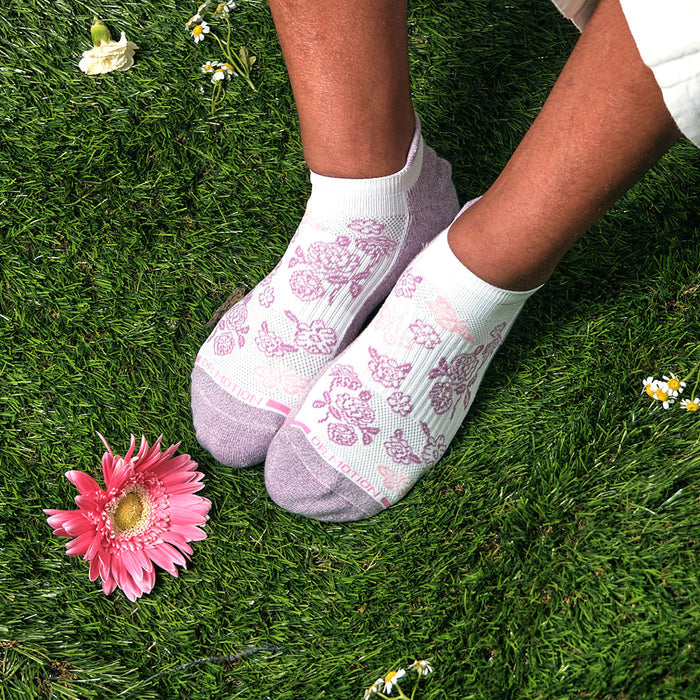 Ankle compression socks with a butterfly and floral design, displayed on grass with a pink flower nearby.