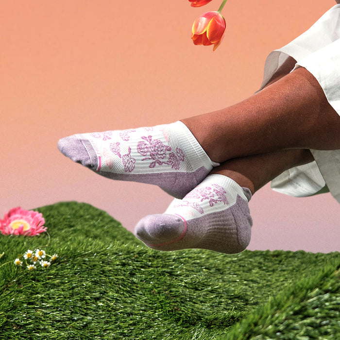 Ankle compression socks with a butterfly and floral design in pink and white, resting on green grass.