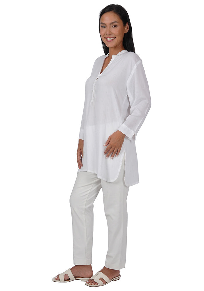 Quarter turn view of a woman wearing a white rayon tunic with 3 buttons, long sleeves, and a loose fit on a white background.