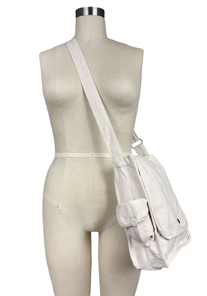 An off-white canvas bag with a button closure and over-the-shoulder strap, displayed on a mannequin against a plain background.