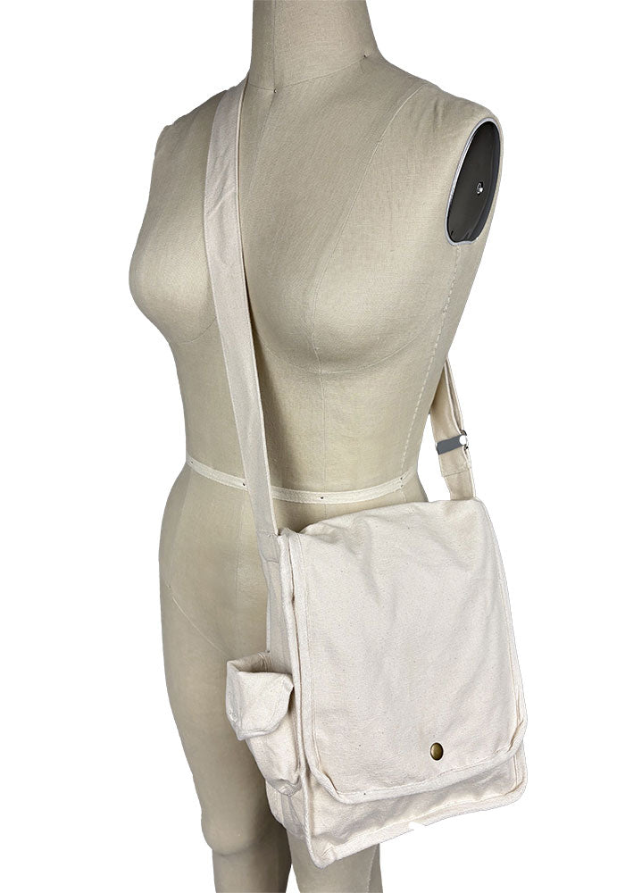 An off-white canvas bag with a button closure and over-the-shoulder strap, displayed on a mannequin against a plain background.