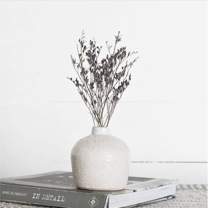 White textured vase with dried branches on a book against a white background. | SW Home