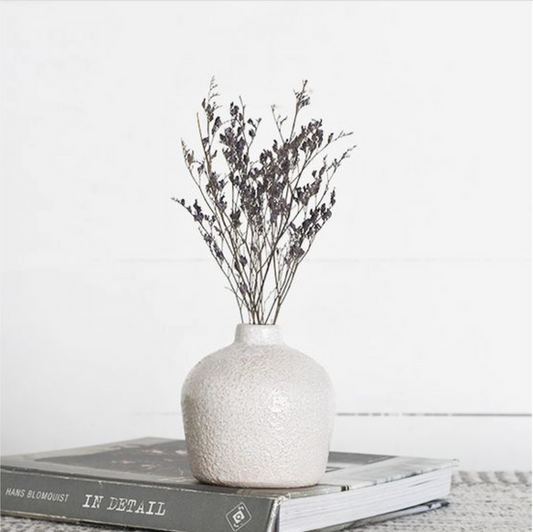 White textured vase with dried branches on a book against a white background. | SW Home