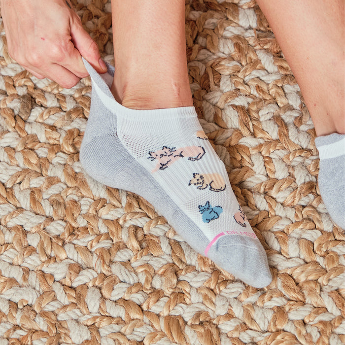 Ankle compression sock being pulled on, featuring a cat design, on a textured woven rug.