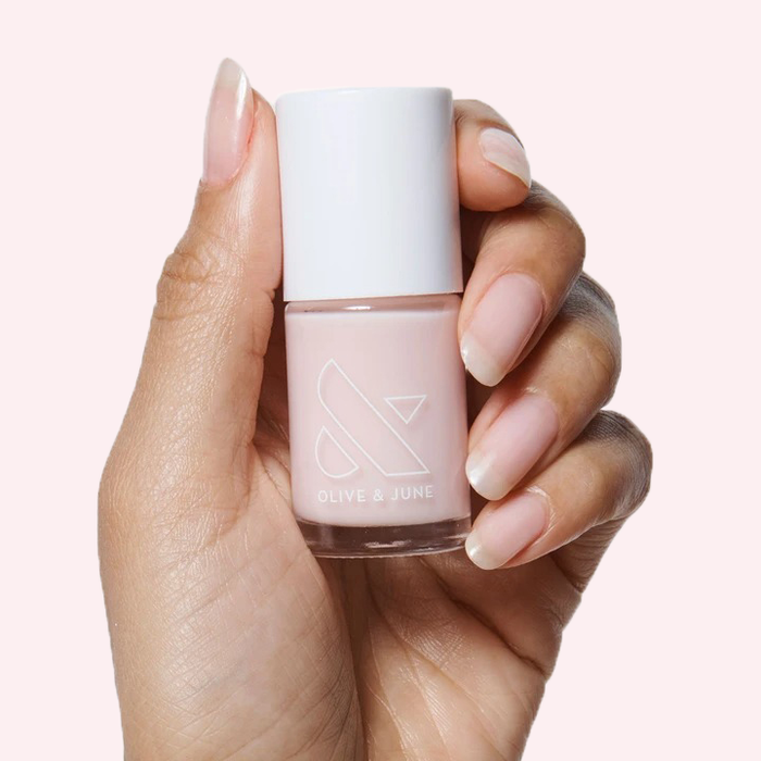 Hand holding a bottle of CCT sheer neutral pastel pink polish with natural nails for a soft manicure look