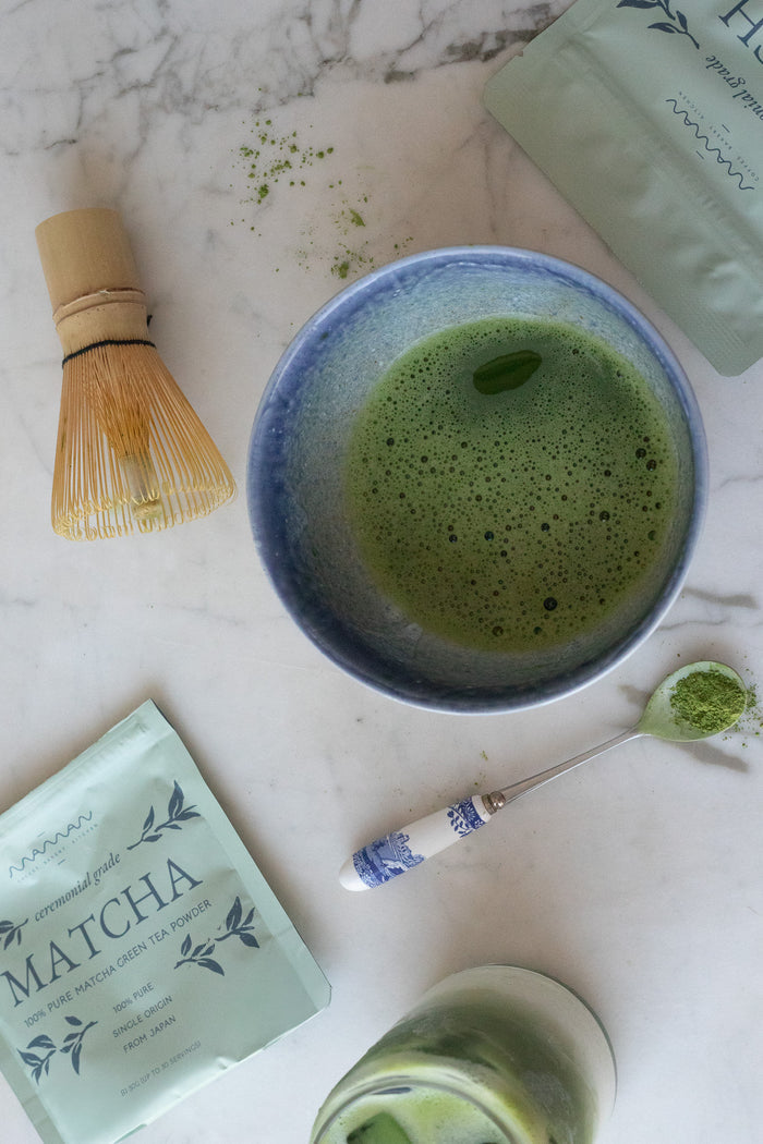 matcha being prepared using the maman matcha powder with bamboo whisk and blue bowl.