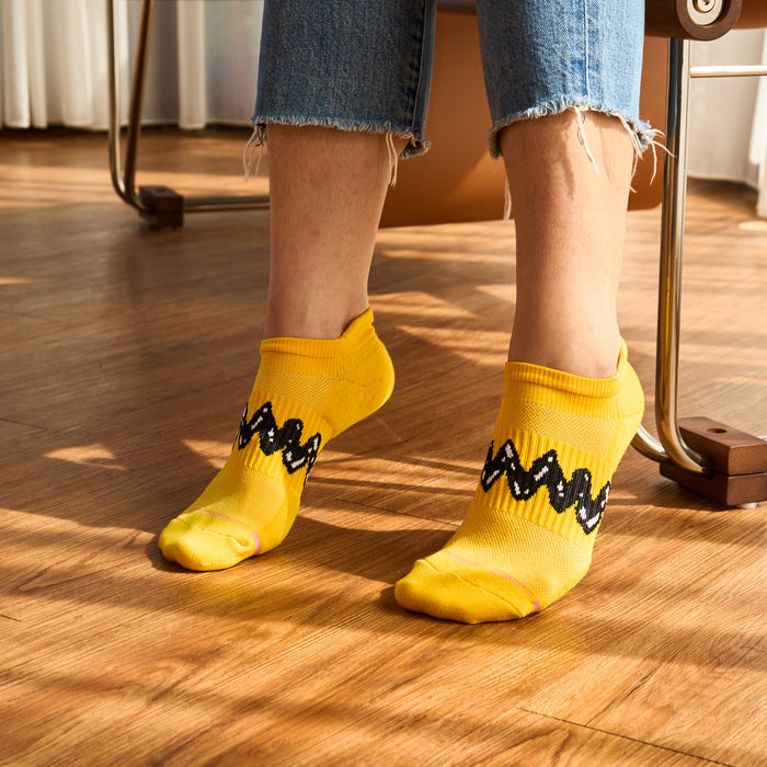 Yellow ankle socks with a black zigzag pattern, worn with cropped jeans on a wooden floor.