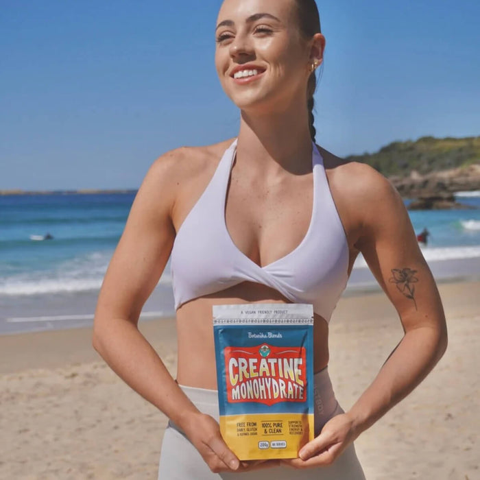 Woman holding a creatine monohydrate supplement on a beach.