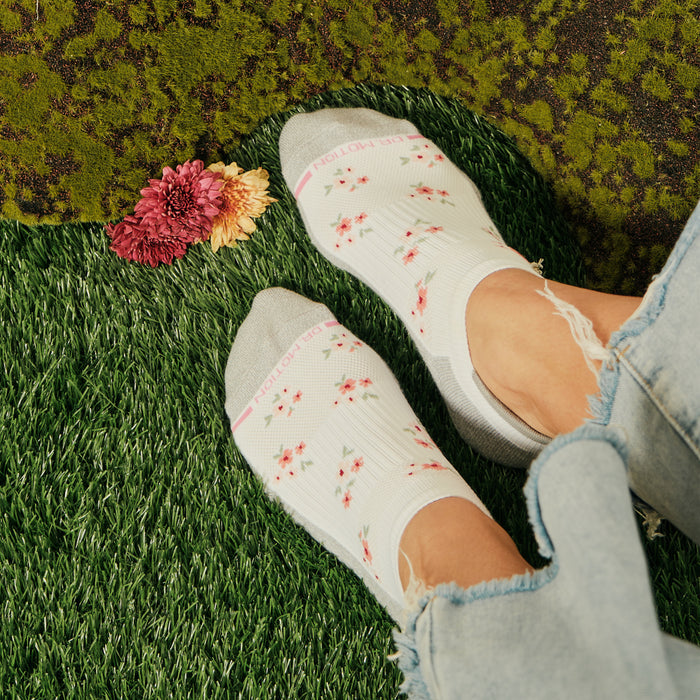 Ankle compression socks with a floral pattern, paired with distressed denim, on a grassy surface.