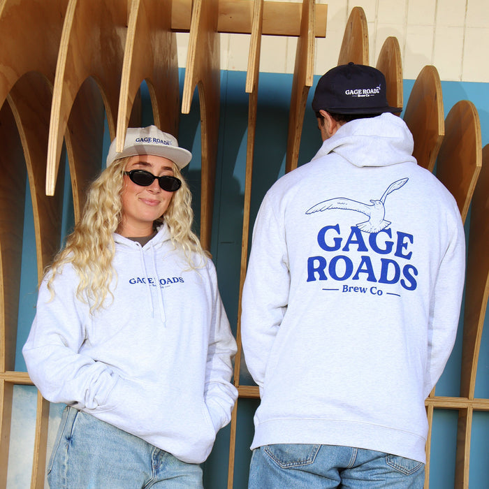 Two people wearing 'Gage Roads' hoodies standing in front of wooden boat hulls.