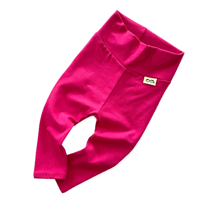 Handmade hot pink baby leggings with a fold-over waistband, displayed flat on a white background. Soft and stretchy for a perfect fit, these gender-neutral baby pants are great for layering with onesies, sweaters, and tees. Available in sizes preemie to 4T.