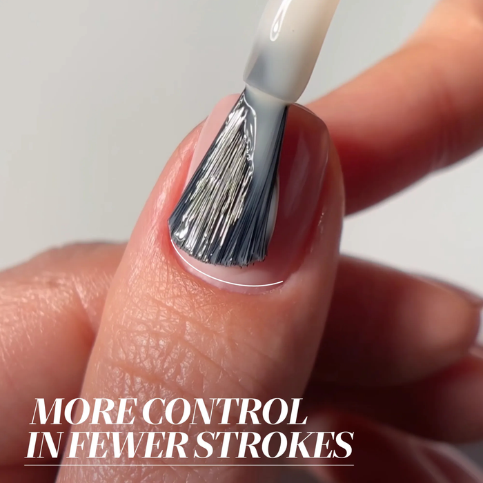A close-up of a brush applying LONDONTOWN Isla Bonita nail polish to a fingernail, with "More control in fewer strokes" in the corner and a hint of shimmering gold reflecting on the nail.