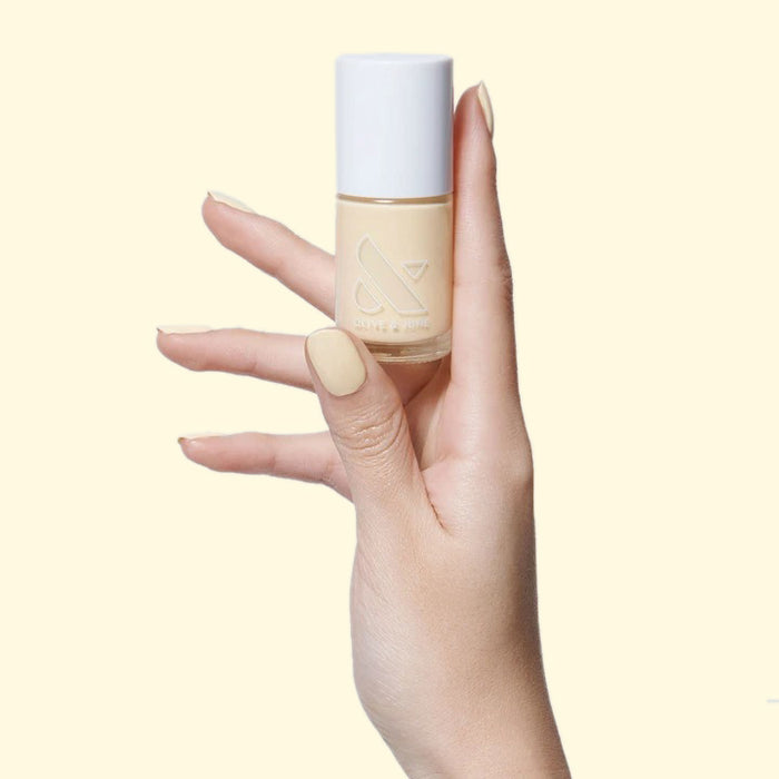 Hand holding JLR nail polish bottle with nails painted in pastel sunny yellow for a bright mani by Olive and June