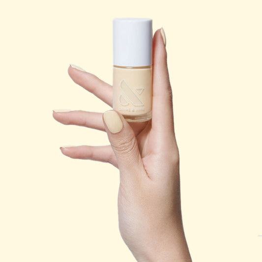 Hand holding JLR nail polish bottle with nails painted in pastel sunny yellow for a bright mani by Olive and June
