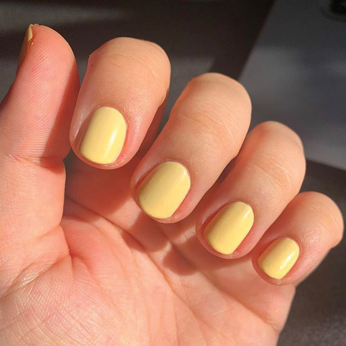 Hand with nails painted in JLR gel polish soft sunny yellow for a bright and smooth mani by Olive and June