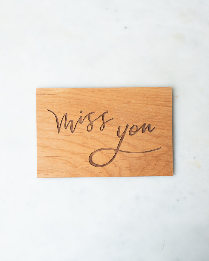 Wooden postcard with “Miss you” engraved in a calligraphic script.