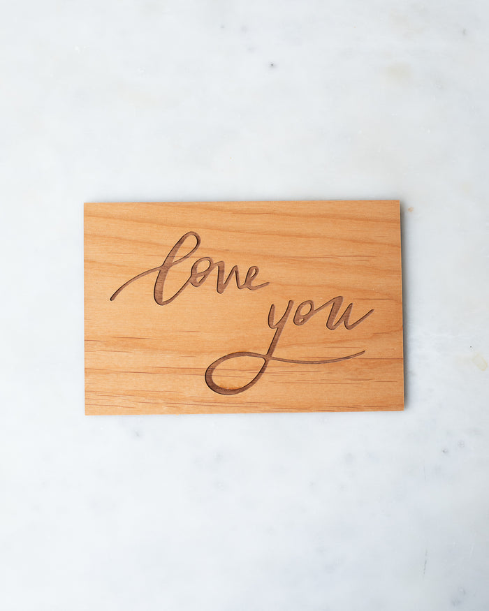 Wooden postcard with “Love you” engraved in a calligraphic script.