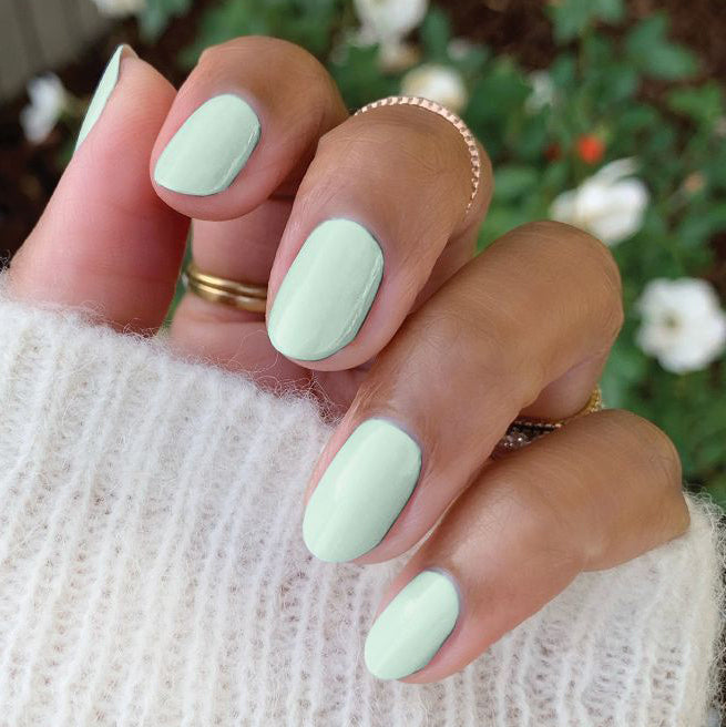 Hand with nails painted in soft sage green KMC gel polish showcasing a smooth, long-lasting manicure in natural light