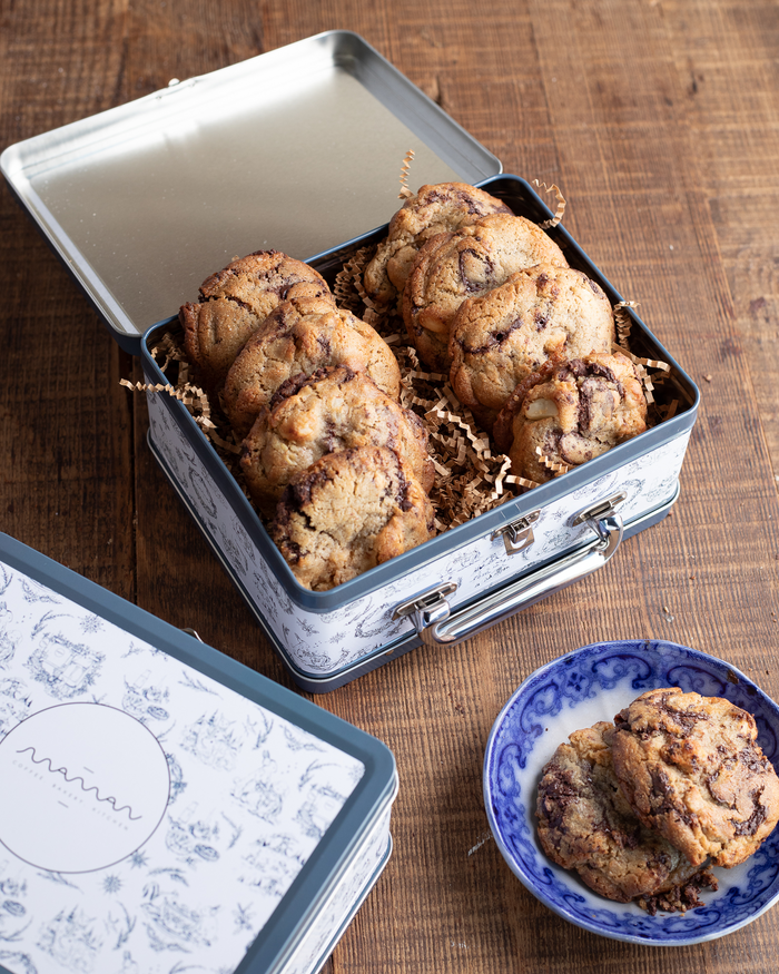 Blue and white toile tin lunch box filled with chocolate chip cookies, with a few cookies placed on a small blue and white plate beside the lunch box.