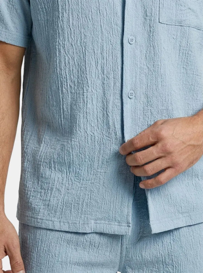 Men's crinkle fabric two-piece set with relaxed camp collar shirt and elastic waist shorts, displayed on a hanger.