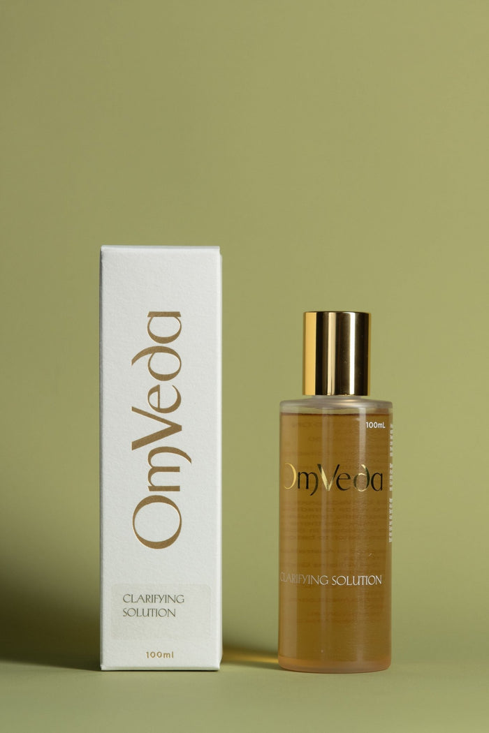 OmVeda clarifying solution bottle with gold cap and amber liquid, plus white box