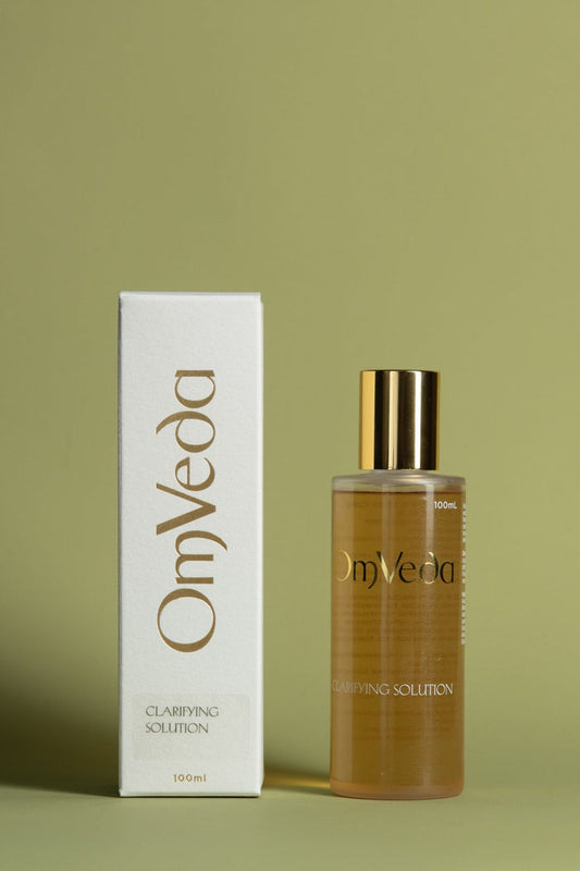 OmVeda clarifying solution bottle with gold cap and amber liquid, plus white box