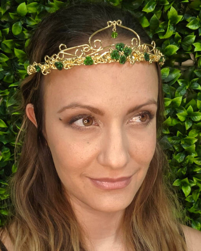 Model wearing Royal Rose Crown gold floral headpiece with green rose accents and crystal drop, front view.