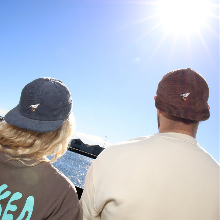 Two people wearing hats and casual clothing, looking out over water with a clear blue sky.