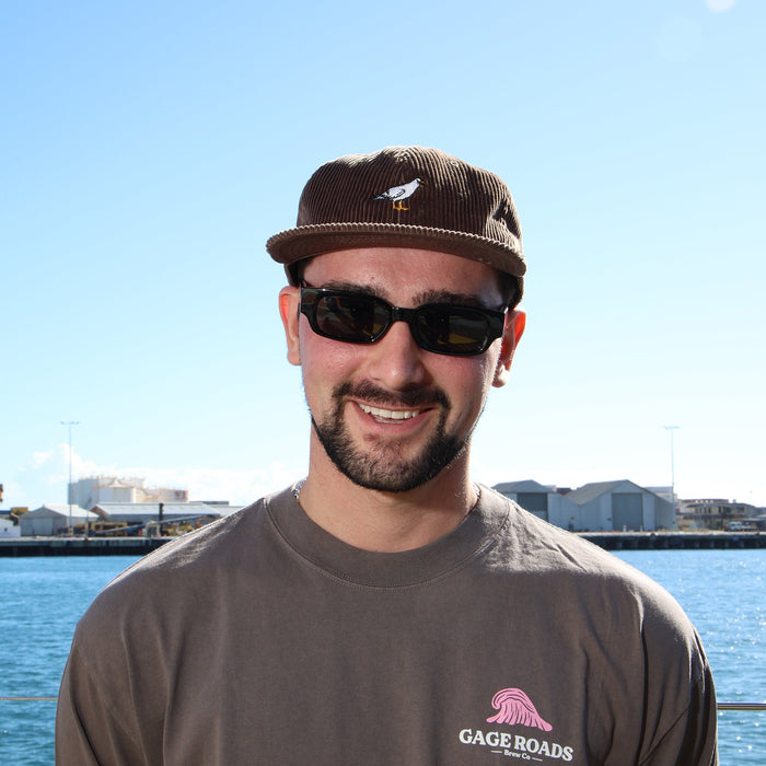 Man wearing sunglasses and a cap with a logo on a waterfront background
