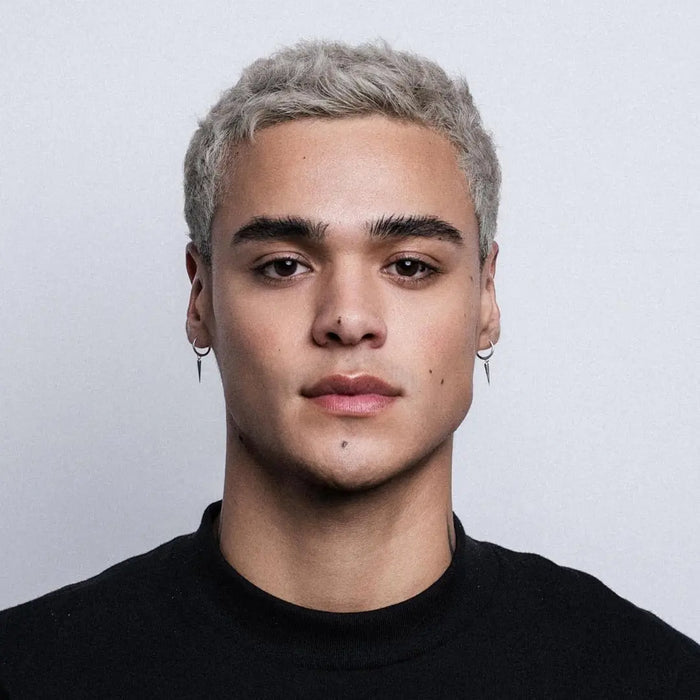 Person with short, styled hair wearing a black shirt against a plain background