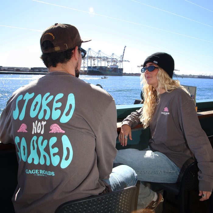 Two people sitting on the port with one wearing a shirt that says 'Stoked Not Soaked'.