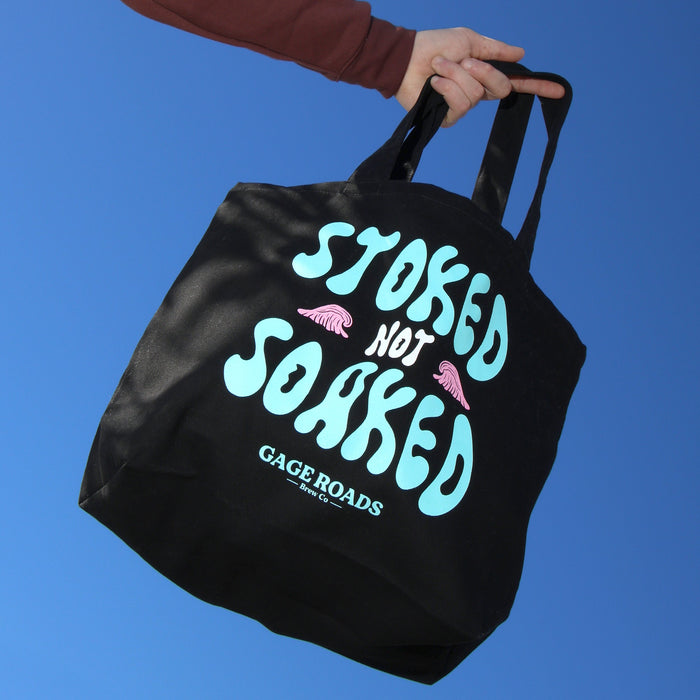 Black tote bag with colorful text against a clear blue sky