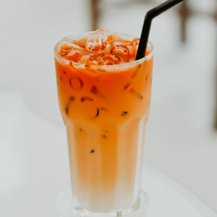 A glass of Thai tea with cream on top and a straw, representing the fragrance oil's connection to the scent of the beverage.