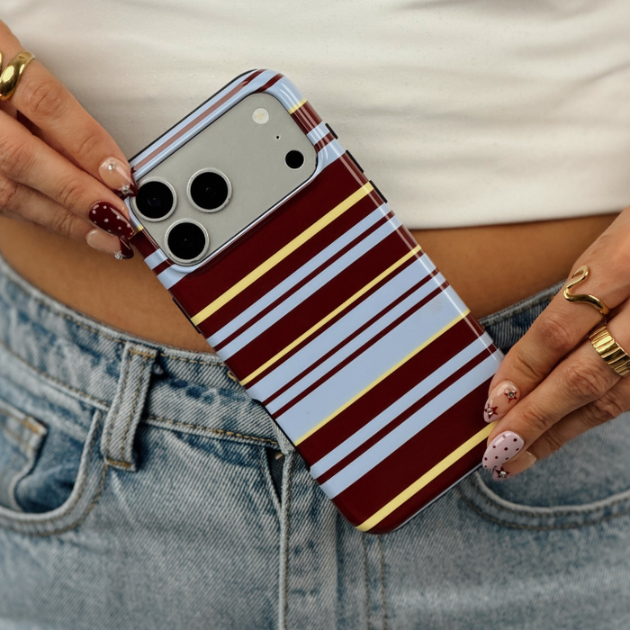 A close-up of a person wearing a white ribbed crop top and light-wash blue jeans, holding an iphone with brown, blue and yellow horizontal stripes.
