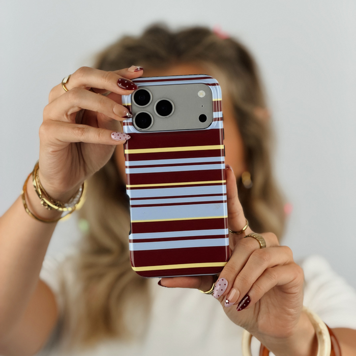 A close-up of a person holding an iphone with a brown, blue and yellow striped phone case.