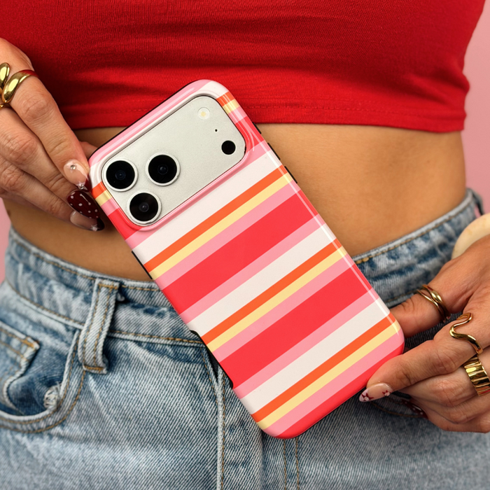 A close-up lifestyle shot of a person wearing a red crop top and blue jeans, holding a phone. The phone is fitted with a protective case featuring a retro striped pattern in shades of pink, orange, yellow, and white.
