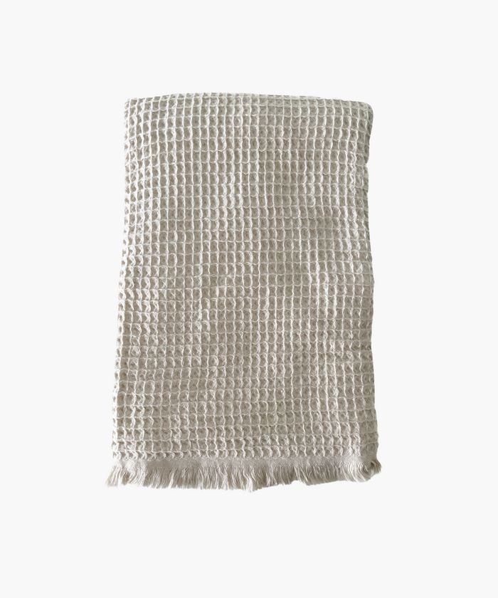 Beige waffle-textured throw blanket with fringed edges, laid flat. The soft material conveys a cozy, inviting feel. Suitable for any living room or bedroom. | SW Home