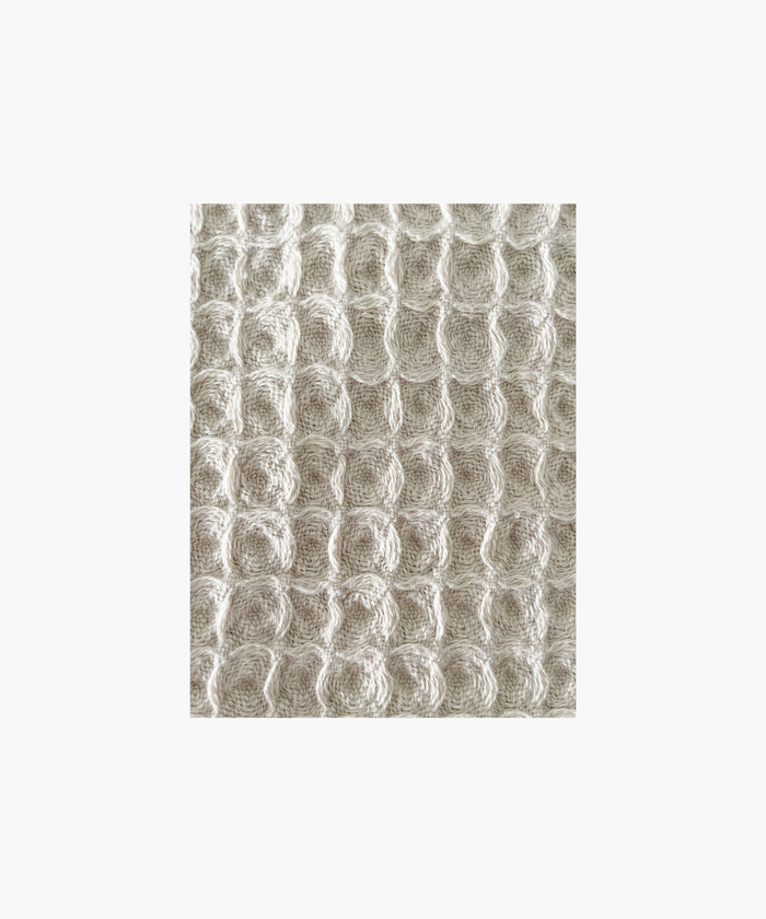 Close up of the beige waffle-textured throw blanket highlighting the texture and color. The soft material conveys a cozy, inviting feel. Suitable for any living room or bedroom.