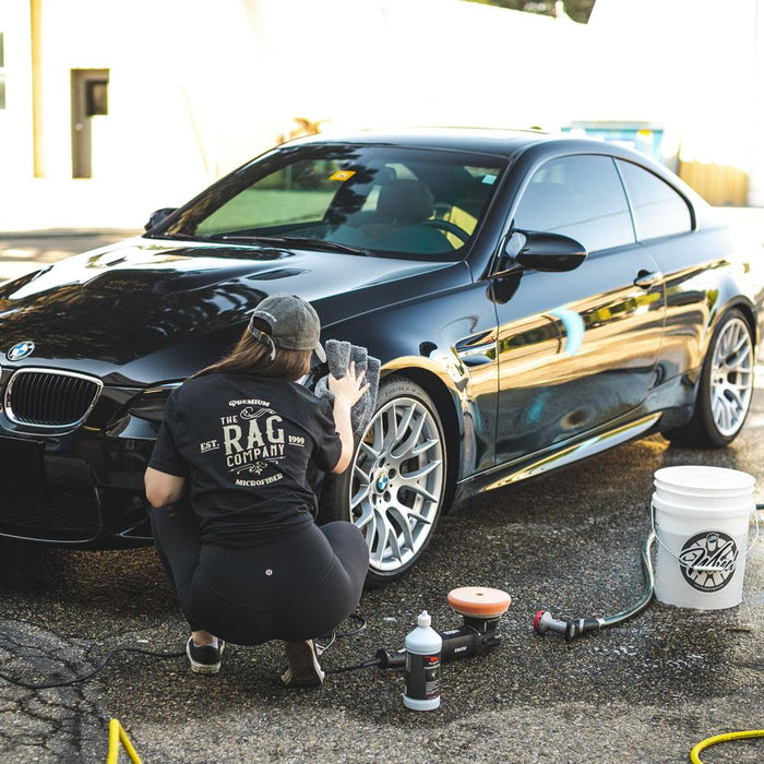 A person cleaning a black BMW coupe with a grey towel while wearing a rag company t-shirt.