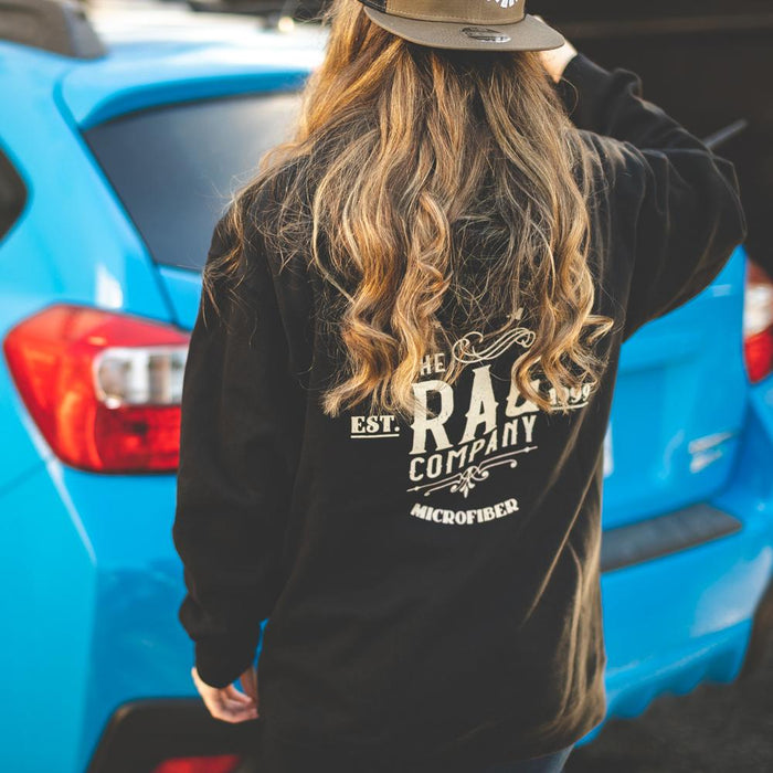 A person wearing a Rag Company black sweater with a blue car in the background.