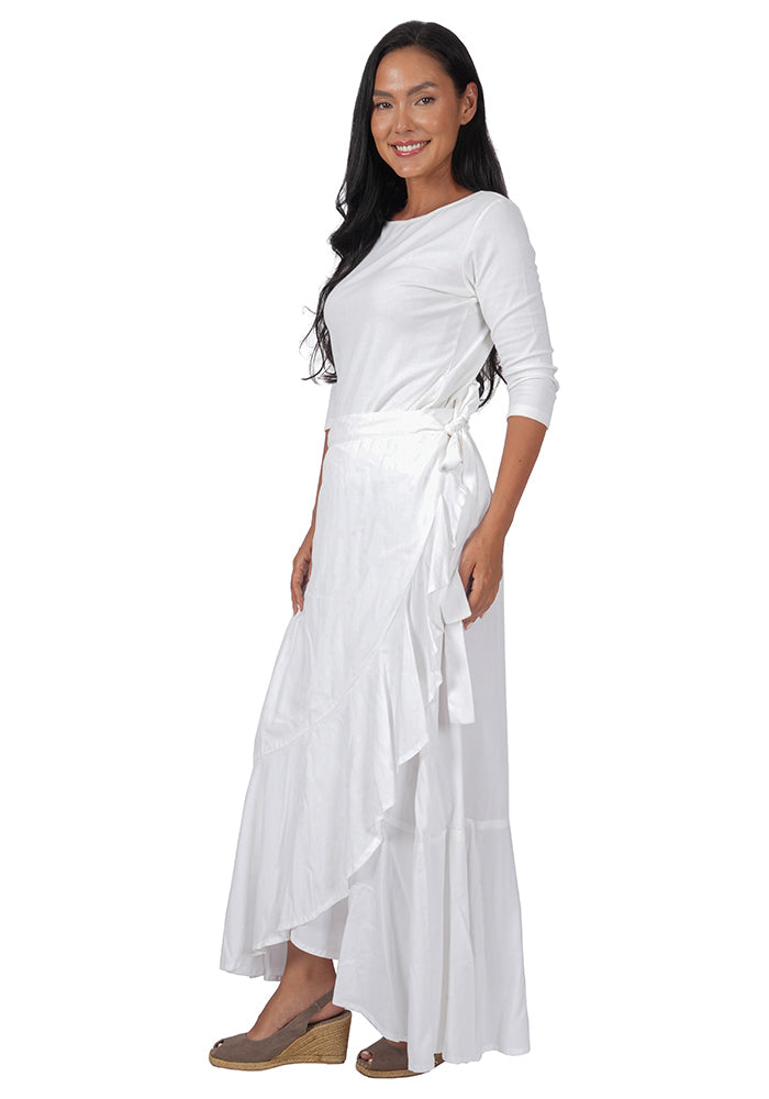 Quarter turn view of a woman wearing a white top with an ankle length, side-tied, flowing white skirt on a white background.